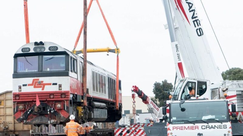 Crane with stabilising pads, lifting a train using specialised hook and slings